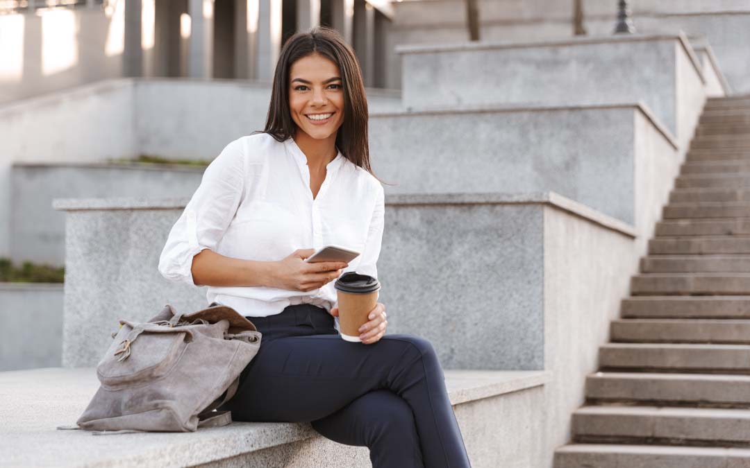 Happy business woman sitting outside with coffee and phone